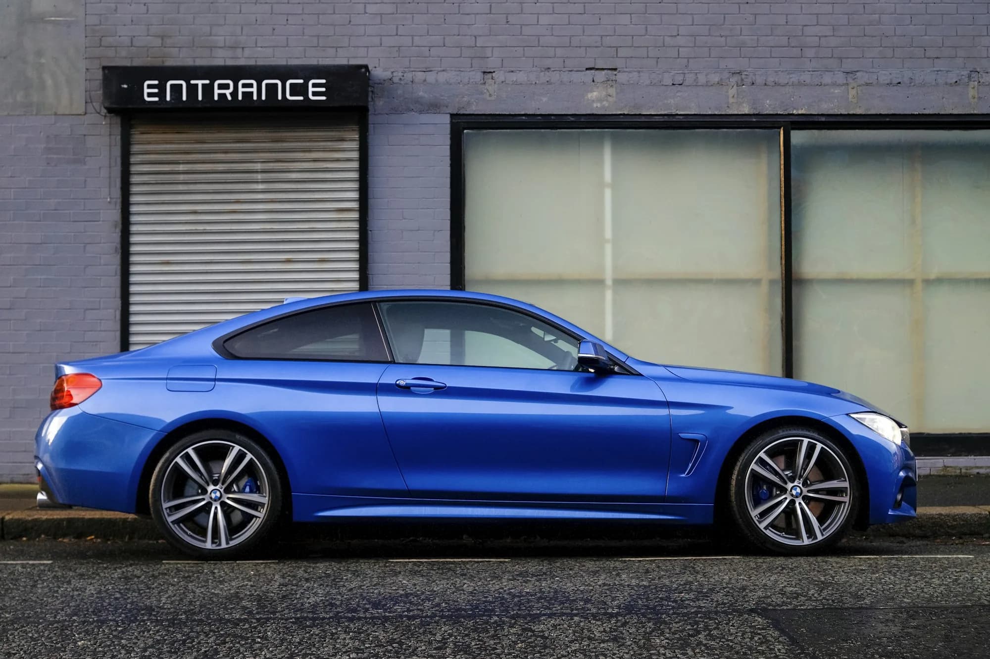 Granatowe coupé BMW zaparkowane przy krawężniku przed halą warsztatową.